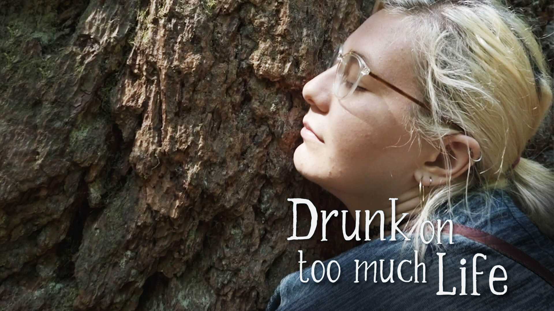 A blonde woman with glasses presses her cheek onto a tree trunk. The title Drunk on Too Much Life appears on the image.