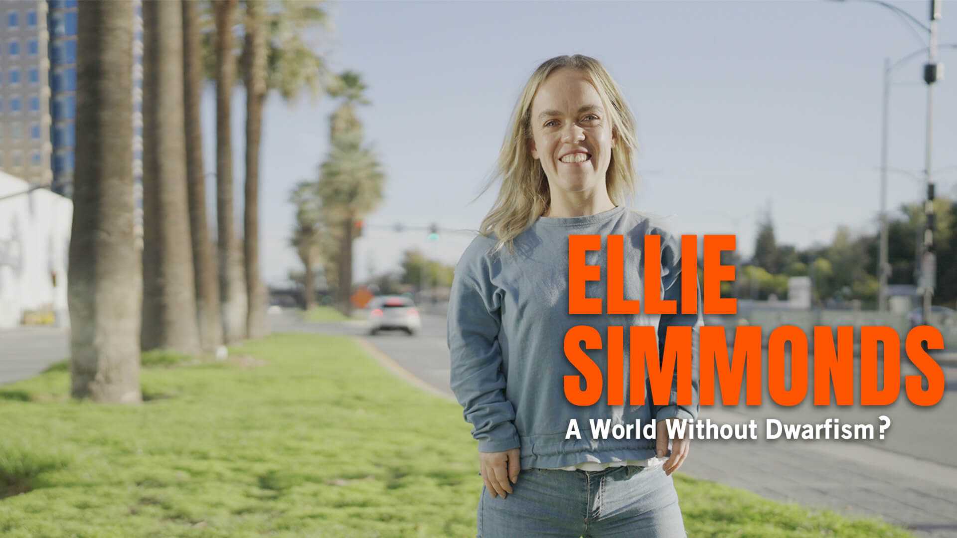 Paralympian Ellie Simmonds, who has dwarfism, stands on a palm tree lined boulevard facing the camera with a big smile.